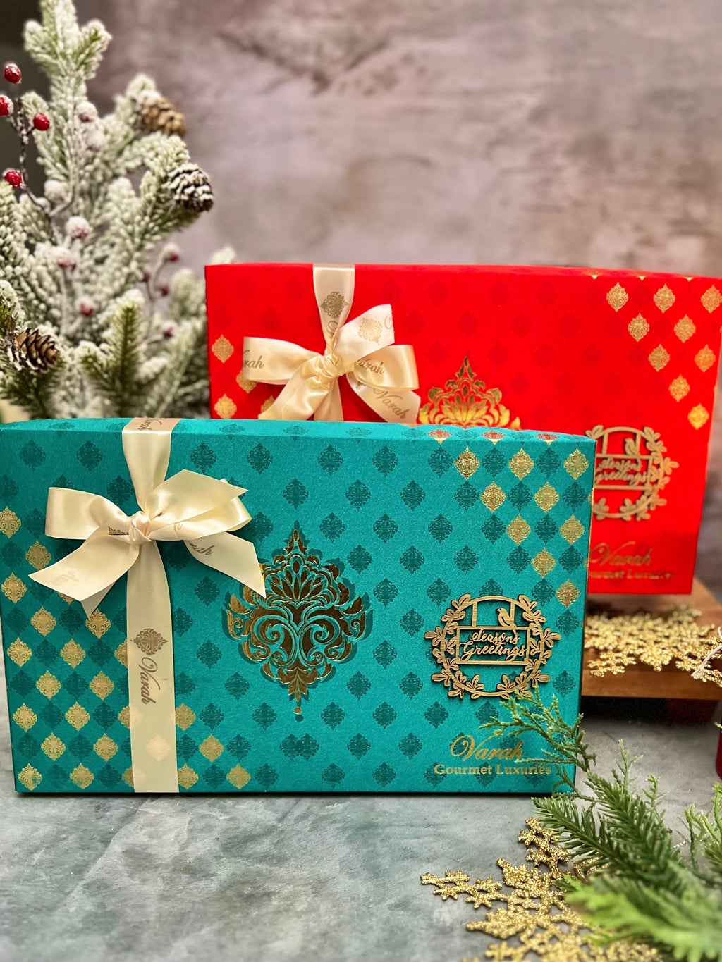 Red and teal Majestic holiday gift boxes with gold patterns and cream ribbons.