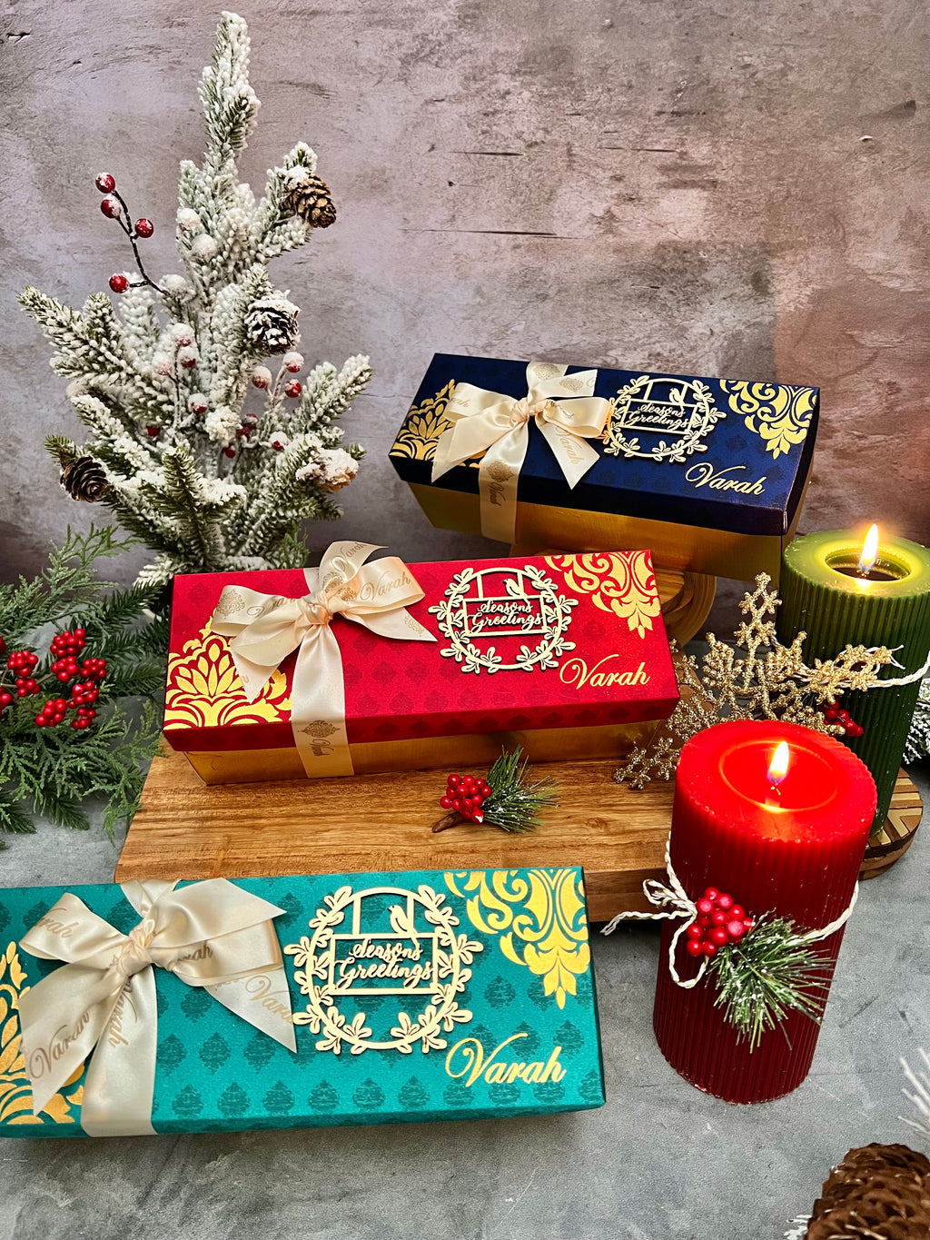 Red, blue and teal Varah holiday gift boxes with cream bows and Season’s Greetings decorations.