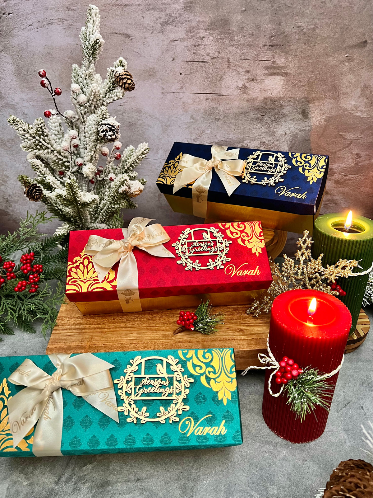 Red, blue and teal Varah holiday gift boxes with cream bows and Season’s Greetings decorations.